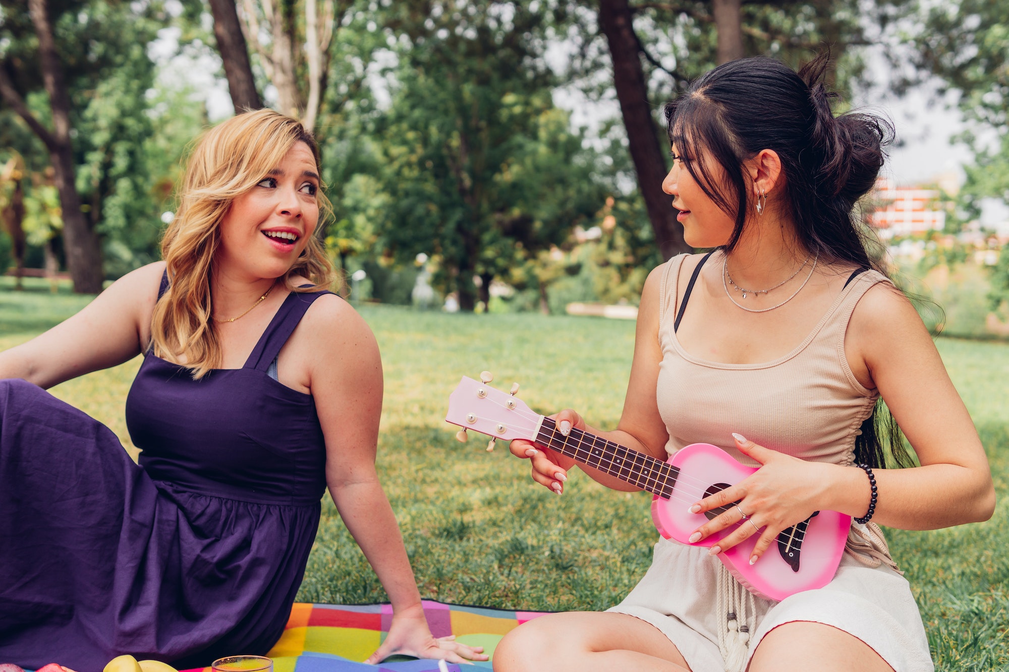 Female friends playing ukulele and singing in park